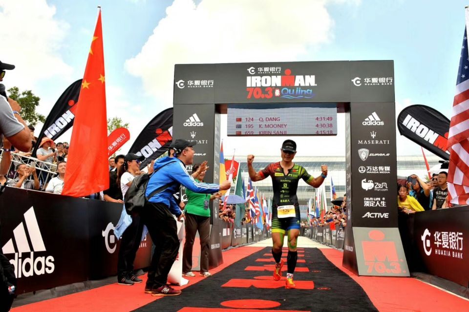 An athlete crossing the finish line surrounded by race signage and branded barriers