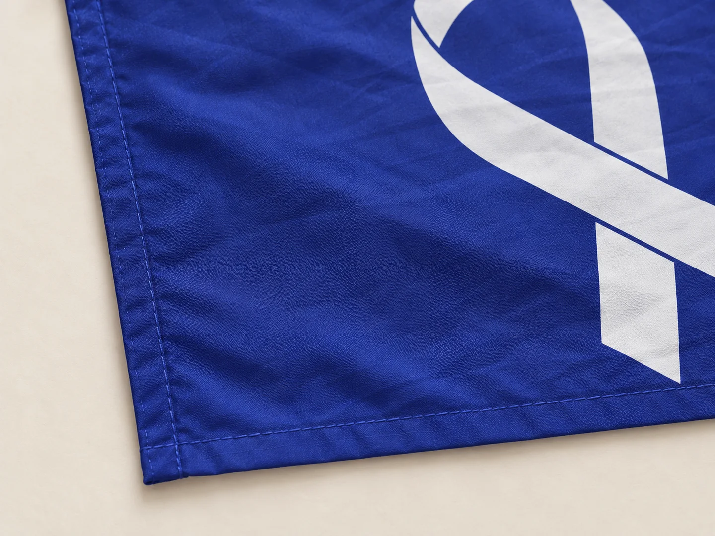 Design presentation close-up of the blue banner stitched hem and edge of its ivory printed graphic