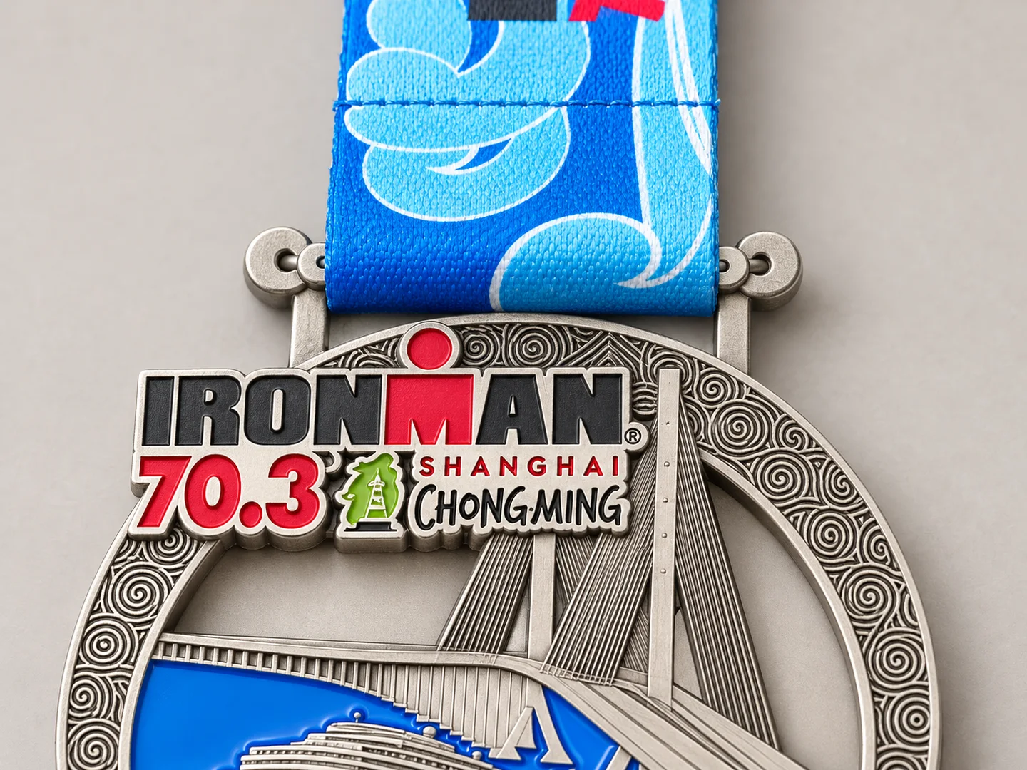 Design presentation close-up of the finisher medal top and its blue woven ribbon attachment