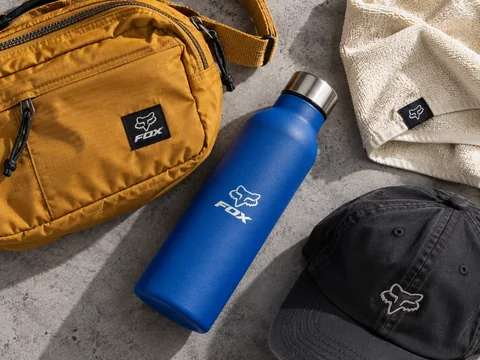 AI-generated FOX merchandise concept with an ochre sling bag, blue bottle, embroidered black cap and cream towel
